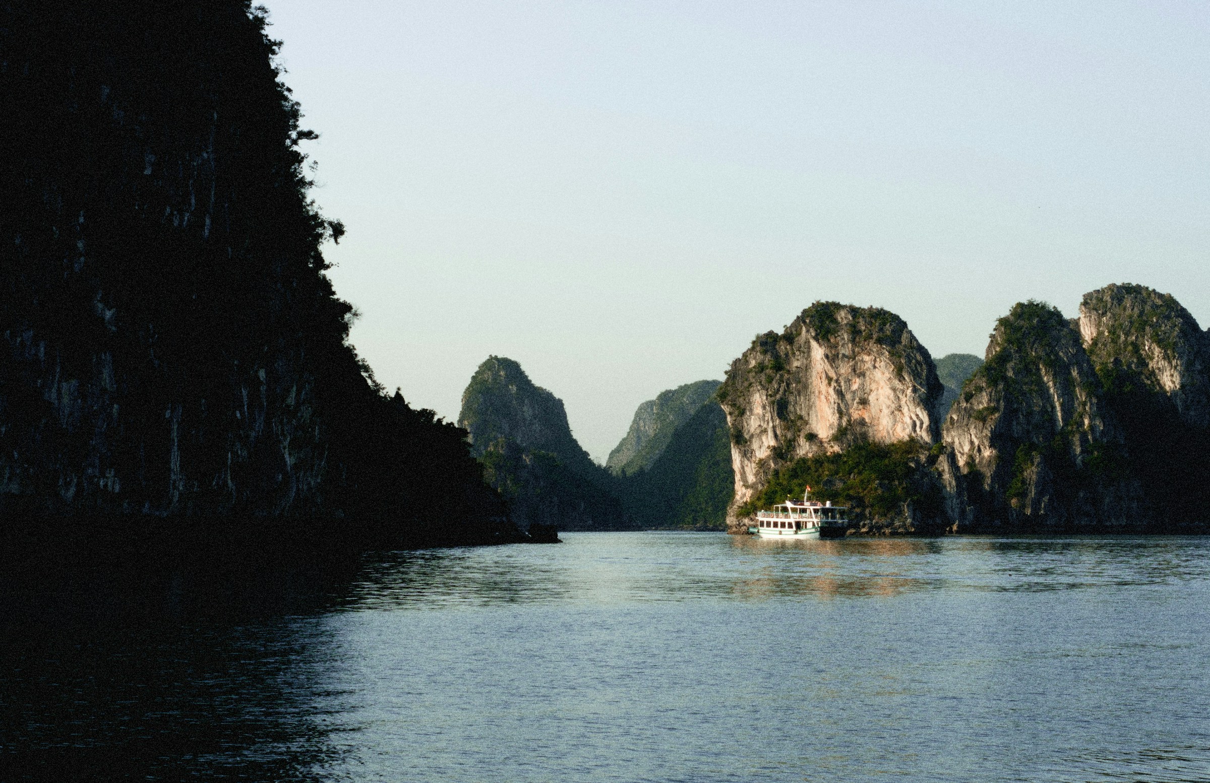 Limestone karsts rising from the water with a boat, Halong Bay
