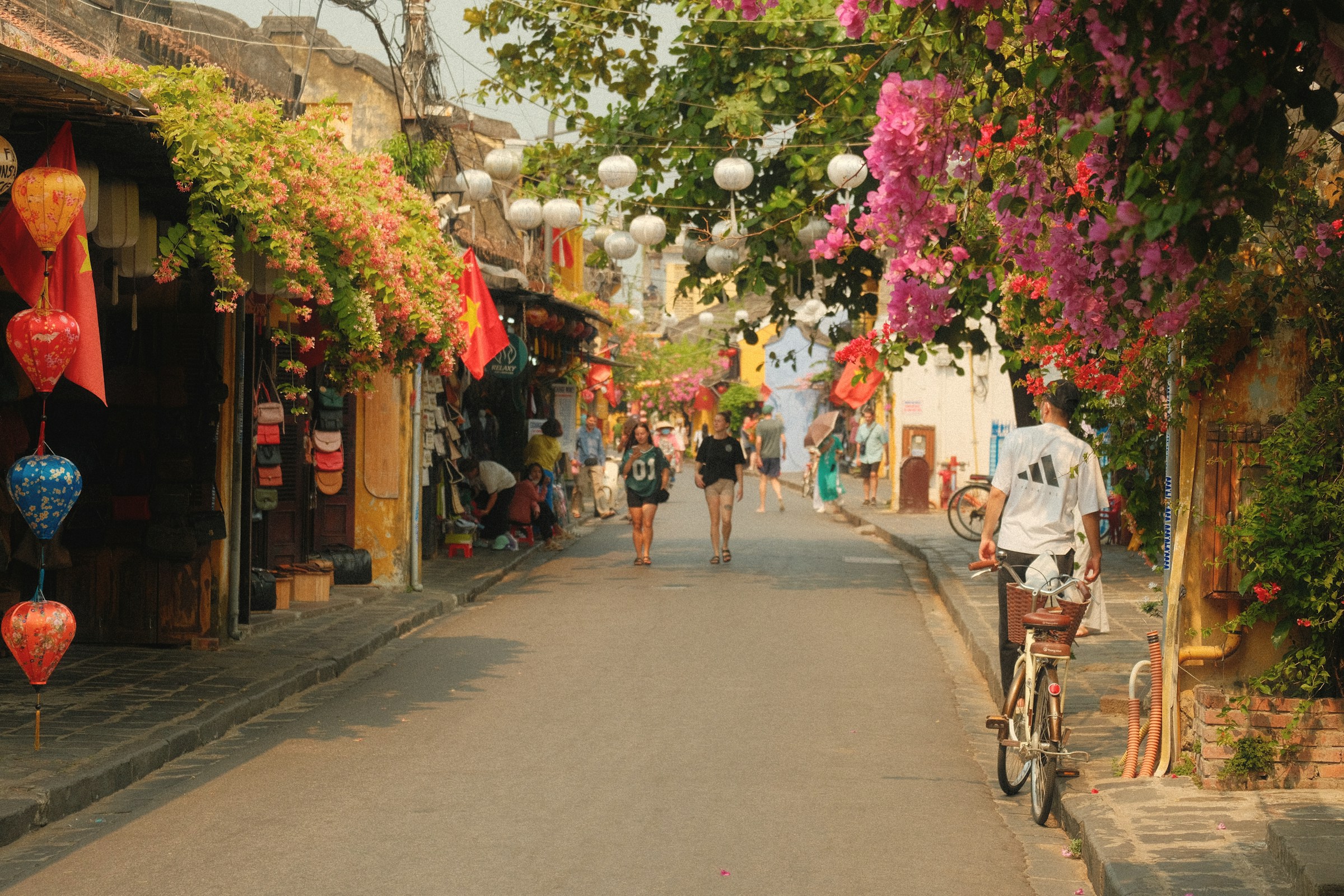 People walking and cycling down a vibrant street market, Hoi An