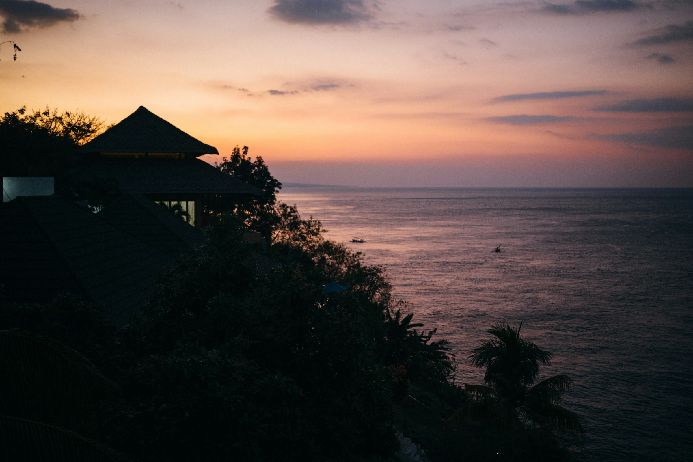 Sunset over the ocean with a house on a cliff