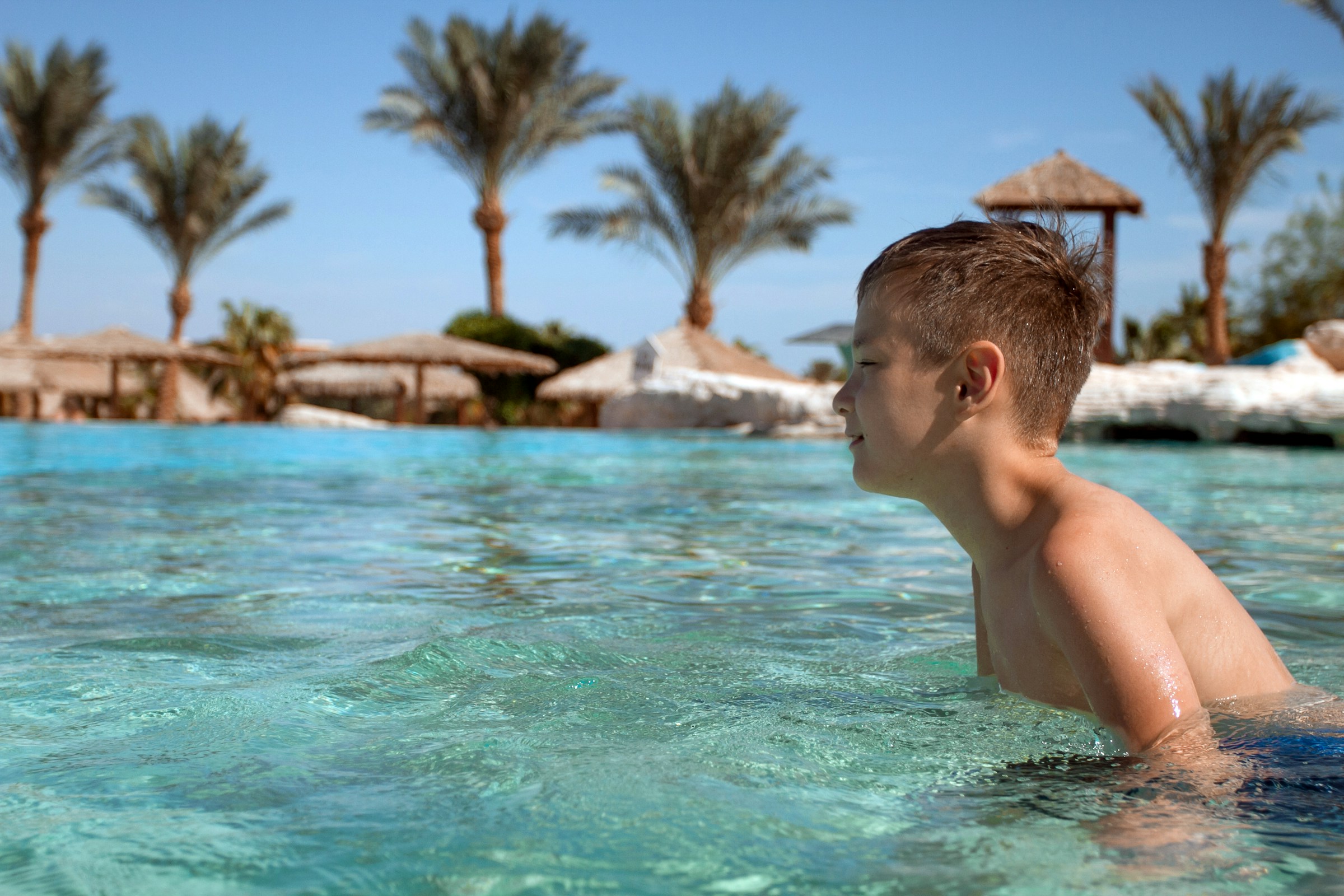 Young boy swimming in a pool with palm trees